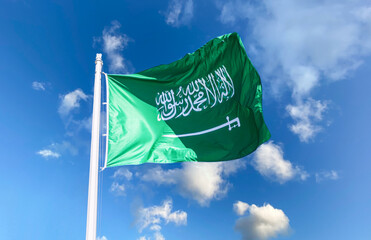National flag of Saudi Arabia waving in the wind against a blue sky with clouds