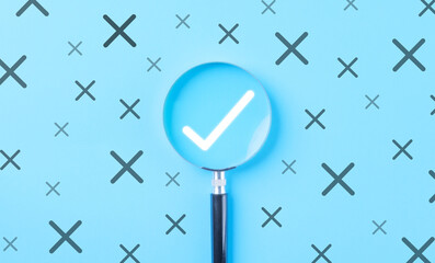 A magnifying glass emphasizing a white check mark among crossed out icons on a blue background....