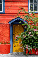 Fototapeta na wymiar Red building with yellow front door and pink flowers.