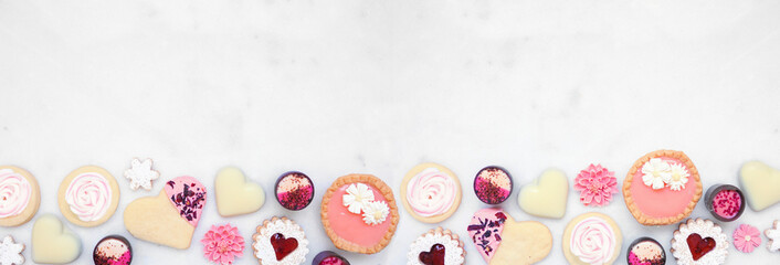 Mothers Day or love themed baking bottom border with a selection of cookies and sweet treats. Top down view on a white marble banner background with copy space. - obrazy, fototapety, plakaty