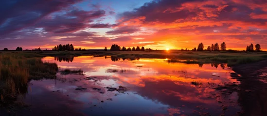 Gordijnen A picturesque sunset over a tranquil lake, with the sun reflecting in the water creating a stunning natural landscape with colorful afterglow in the dusk sky © AkuAku