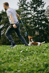 Caucasian man plays toy rope tug-of-war with a dog on green grass. An active spring walk in park of...