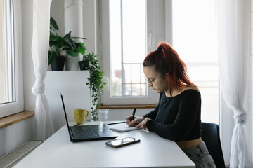 Young female student using laptop and notebook, studying  at home 