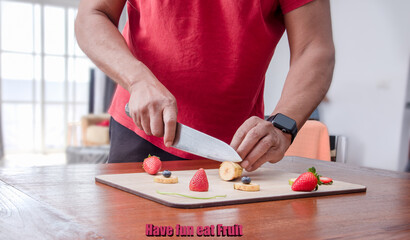 Man cutting fresh strawberries and bananas with a knife on a wooden board ,a fun way to motivate kids to eat fruit .Text : have fun eat fruit