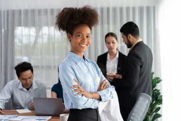 Young African businesswoman poses confidently with diverse coworkers in busy meeting room...
