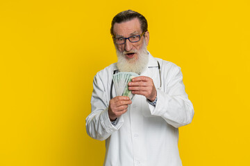 Rich happy senior doctor cardiologist man waving money dollar cash banknotes bills like a fan,...