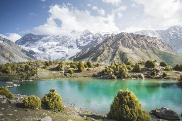 Fototapeta na wymiar Panorama of mountain ranges and turquoise cold mountain lake on a warm sunny evening in the Fan Mountains in Tajikistan, Tien Shan highlands in the evening