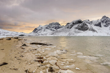 Lofoten Islands in Norway and their beautiful winter scenery at sunset. Idyllic landscape on snow covered beach. Tourist attraction in the arctic circle. Nordic travel destination.