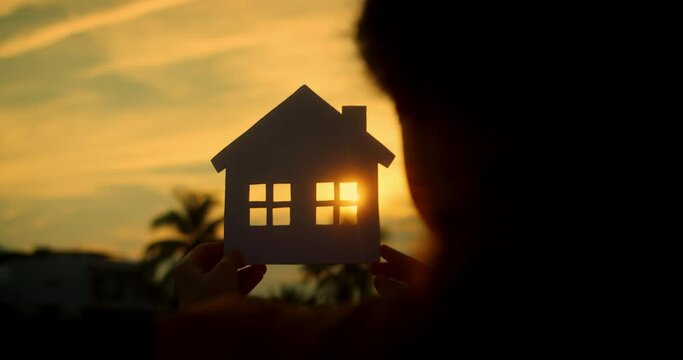 Concept of Happy Family Purchase Property, Home, Life, Insurance, Care, Savings, Mortgage, and Estate.Symbol happiness. Child little girl male hands holding model of a paper house on sunset background