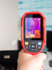 Thermal imaging examination of a work area with a computer desk and laptop. A cold bridge on the adjacent wall.