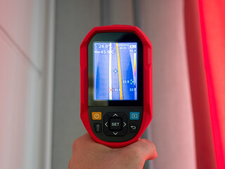 A thermal imaging camera held in the man hand on a warm radiator pipe. Close up vertical image.