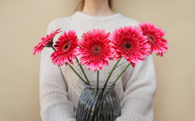 a girl holds a vase with a bouquet of pink gerberas. holiday concept