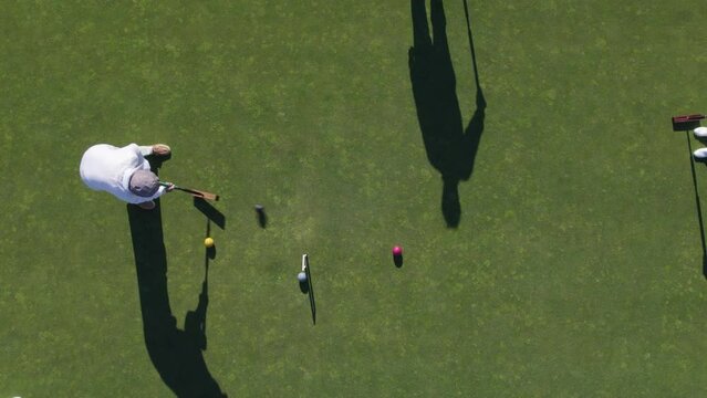 Playing croquet. Aerial view of a player in a croquet course in green lawn, slow motion, preparing and hitting the ball  (Drone shot, 4K ) 