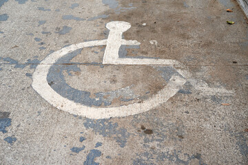 A close-up image capturing a faded and weathered handicap parking sign painted on the asphalt. The...