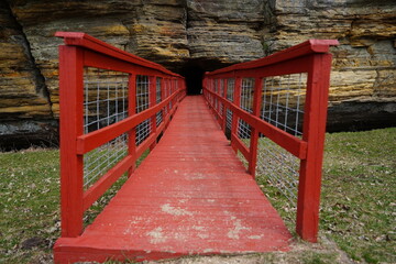 Fototapeta na wymiar A red man-made bridge leads into a rock tunnel at Pier County Park in Rockbridge, Wisconsin a Native American historical site.