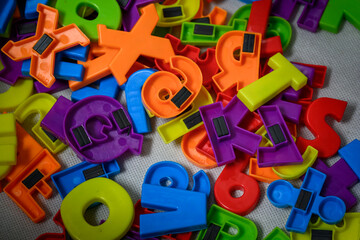 Brightly colored plastic alphabet pieces with magnets to stick to a metal board.  Kids toys are put...