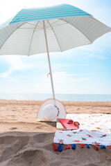 Parasol with hat, sunglasses, pink diary and towel on a splendid bright beach in summer without...
