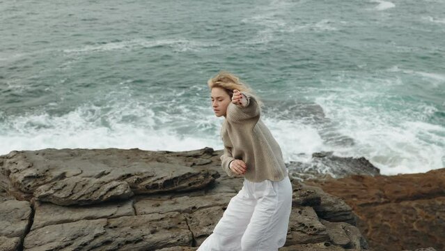 A serene image capturing the essence of a woman dancing freely on a rocky shore with waves crashing in the background, embodying coastal rhythm.