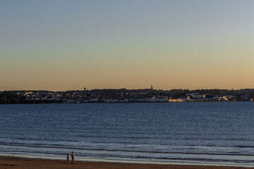 Serene Beach Walk at Sunset with Distant Cityscape