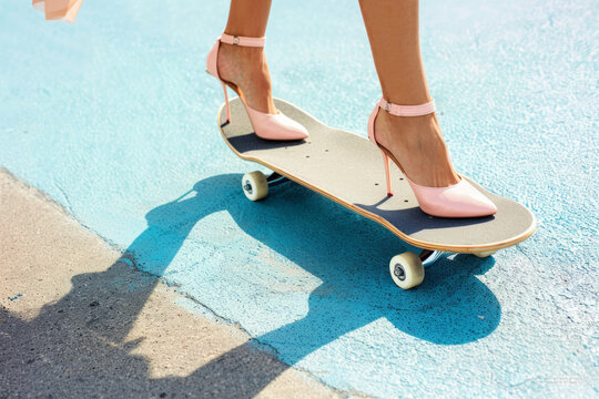 woman legs in pink high heels on skateboard on blue asphalt