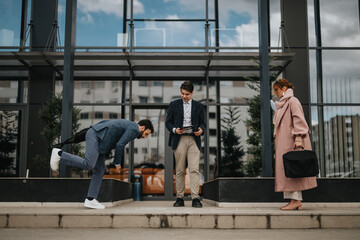 Young male business person stumbling while walking on a sidewalk, his colleagues are looking at him.