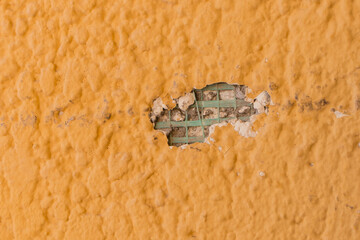 Hole in the wall close-up ruined broken damaged construction texture of bright yellow surface