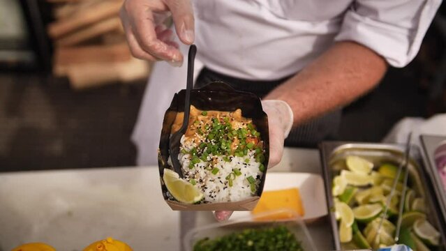 A cook serving curry rice with lime in paper bowls at a street food stall. Curry street food. A cook putting curry on a takeaway. 