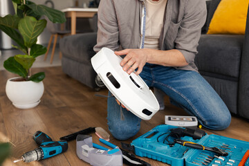 man cleans the container for garbage and dust from a robot vacuum cleaner. a man in blue jeans and...