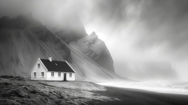  A monochrome image depicts a house perched atop a mountain, framed against a somber sky