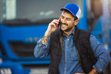 Happy confident male driver standing in front on his truck, using his phone to talk to someone