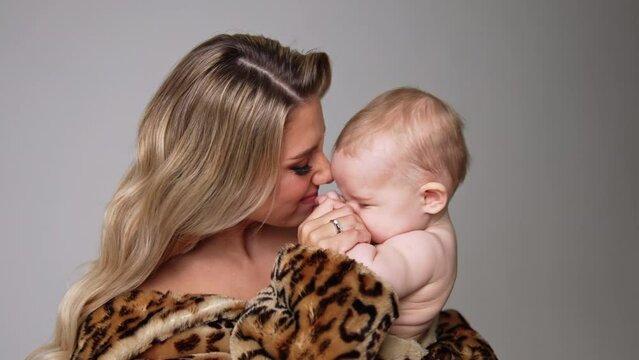 Young beautiful mother with her adorable child. Caring and loving mom kisses her kid and plays with him. Close up. White backdrop.