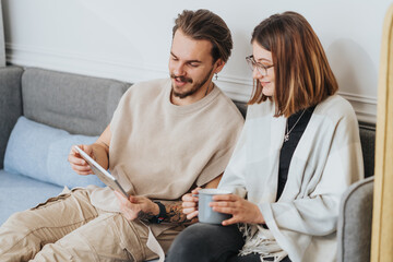 Casual couple with tablet smiling on couch.