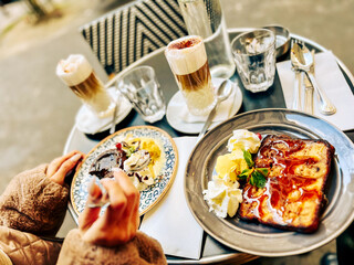 Hands of a woman holding a cup of cappuccino with chocolate cake and ice cream in Paris cafe, France