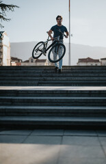 A casual man carrying his bicycle down the steps in an urban park during the daytime.