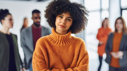 Fototapeta premium A young adult multi-ethnic woman wearing an orange turtleneck sweater, standing in the middle of the office surrounded and stared at by work colleagues, deep in thought and daydreaming