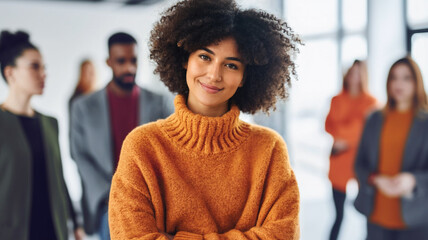 young adult multi-ethnic woman wearing an orange turtleneck sweater, standing in the middle of the office surrounded by work colleagues, deep in thought and daydreaming, cheering and happy