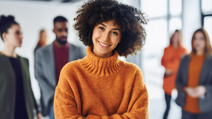 young adult multi-ethnic woman wearing an orange turtleneck sweater, standing in the middle of the office surrounded by work colleagues, deep in thought and daydreaming, cheering and happy