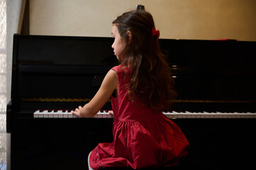 Authentic Caucasian little kid girl musician pianist with beautiful long hair, dressed in elegant...