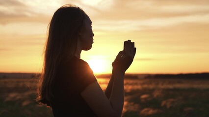 Woman praying with folded hands at sunset silhouette. Faithful girl supplication palms arms folded in worship to god. Religion faith belief spirituality practicing spiritual activities in nature field - obrazy, fototapety, plakaty