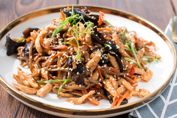 spaghetti wok with soy sauce and meat on a plate with wood mushrooms. the concept of the restaurant...