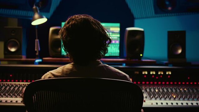 Music engineer producing sounds with mixing console and daw software interface, working on a new album. Technician uses audio console with moving faders and colored meters. Camera B.