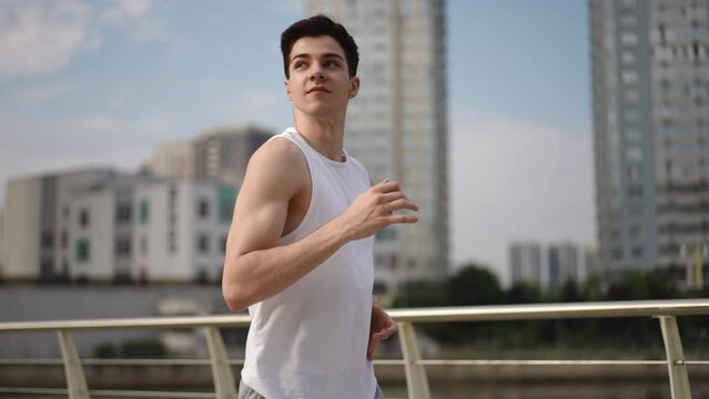 Slow motion. A guy runs outdoors against the background of modern buildings on a summer morning. The guy smiles while morning jog