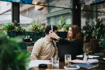A cheerful woman playfully adjusts a man's hair while enjoying a relaxed moment together at a cozy outdoor cafe, surrounded by greenery.