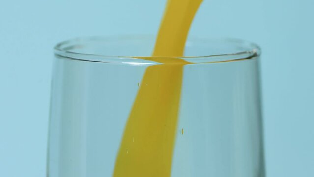 Extreme close-up, low shot, glass jug pouring orange juice into a glass, on a blue background