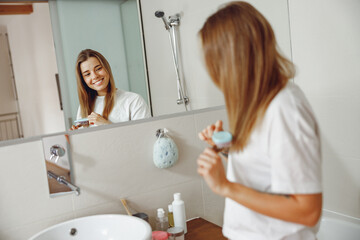 Back view of young woman brushing her hair with comb while standing in bathroom near mirror