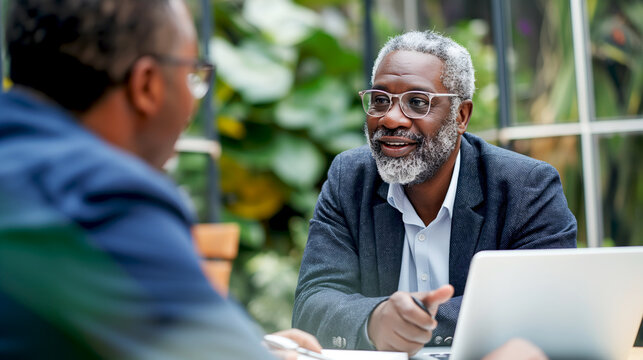 Two professionals engaged in a conversation over a laptop at an outdoor table, with a man gesticulating while explaining a point - Generative AI