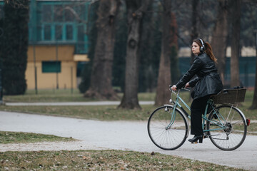 An elegant and confident young businesswoman enjoys a leisurely bike ride through a serene park setting.