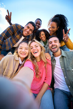 Vertical. Group of multiethnic friends taking selfie with smart mobile phone outdoors. Happy young multiracial people smiling together looking camera. University students having fun in college campus