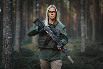 Beautiful military girl with a modern AK 12 rifle in the forest at war.