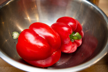 Fresh Red Bell Peppers in Stainless Steel Bowl. Two vibrant red bell peppers in a stainless steel...